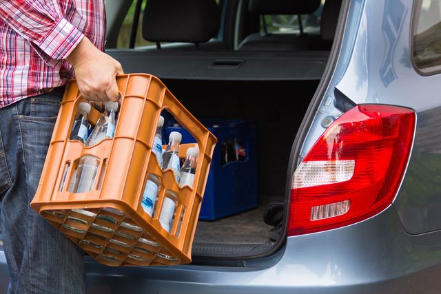 Eine Mehrwegkiste mit Glasflaschen wird in den Kofferraum geladen